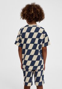 Kortärmad skjorta och shorts set i krämfärg med marinblå rutmönster. Mjuk textur, avslappnad passform och solida sömmar. Ingen synlig hårdvara.