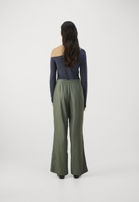Marineblå off-shoulder langermet topp kombinert med løse olivenfargede vide bukser. Glatt tekstur, flytende design, synlig midjebånd.