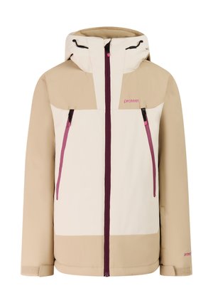 Jonge vrouw die een beige-witte winterjas draagt, magentakleurige broek, roze gebreide hoofdband en zwarte winterlaarzen, staand tegen een effen achtergrond.