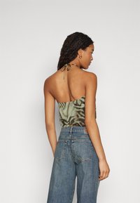 Top cu gât halter în model de camuflaj verde și maro. Fabricat dintr-un material ușor, are un design legat la spate și scurt. Este asortat cu blugi cu talie înaltă.