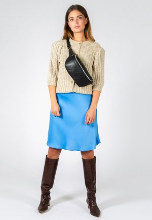 Beige ribbet strik cardigan med grønne knapper, blå satin glidende kjole, sort crossover taske og brune knæhøje støvler med krokodillemønster.