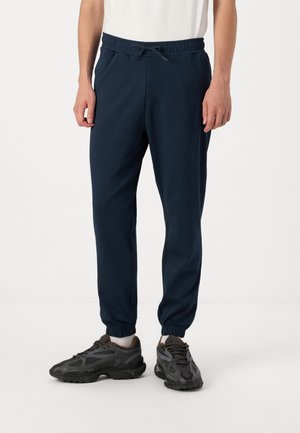 Navy blue jogger pants with an elastic waistband, drawstring closure, and cuffed ankles. Made of soft fabric, paired with dark athletic shoes.