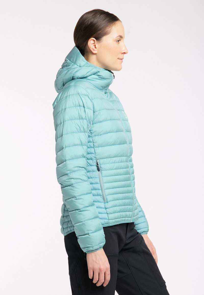 Chaqueta de plumas en color turquesa claro con patrón acolchado, capucha y bolsillo con cremallera en el frontal. Confeccionada con un material suave y resistente al agua.