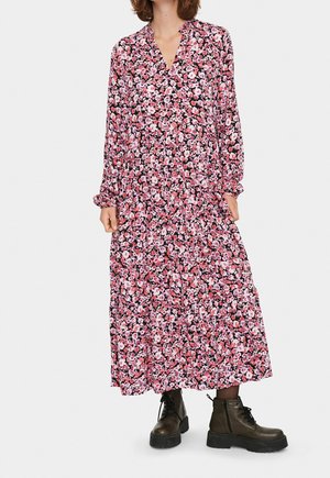 Bloemen lange jurk met een v-hals, voorzien van een roze en zwart patroon, lange mouwen en een gelaagd rok; gecombineerd met donkerbruine laarzen.