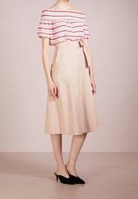 Blusa con los hombros al descubierto de rayas rojas y blancas, combinada con una falda beige hasta la rodilla con un lazo en la parte delantera y un ligero vuelo. Tacones negros.