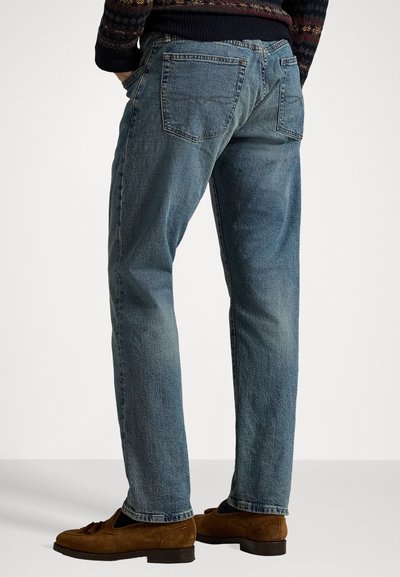 Light blue denim jeans with a straight fit, rear pockets, and subtle fading. Paired with brown suede loafers.