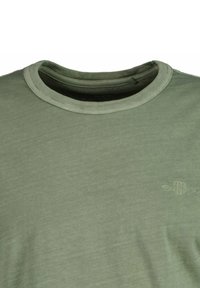 Grön t-shirt med rund hals och subtilt broderad logo på vänster bröst, som visar detaljer om överkroppen och halslinjen.