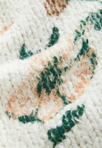 Gros plan sur un tissu à maille épaisse avec des motifs floraux texturés verts et pêche sur un fond blanc.