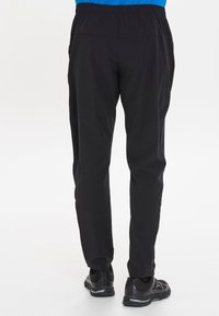 Zwarte sportbroek met een elastische tailleband, taps toelopende benen en een gladde textuur, gecombineerd met zwarte sportschoenen.