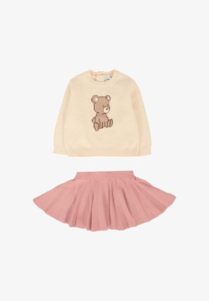 Beige trui met een bruine teddybeerontwerp op de voorkant, gecombineerd met een roze geplooide rok. Beide gemaakt van zachte, gestructureerde materialen.