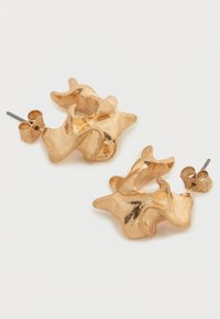 Χρυσόχρωμα αφηρημένα μεταλλικά σκουλαρίκια με υφή κυματιστού σχεδίου. Διαθέτουν καρφωτό κούμπωμα και γυαλιστερό φινίρισμα με αντανακλάσεις φωτός.