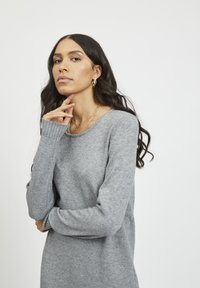 Grå strikkegenser med lange ermer og ribbede mansjetter, med rund hals og myk tekstur. Minimalistisk design, nøytral farge.