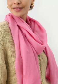 Écharpe tissée rose drapée sur un pull beige texturé, présentant un tissu doux et léger ainsi qu'une forme ample et fluide.