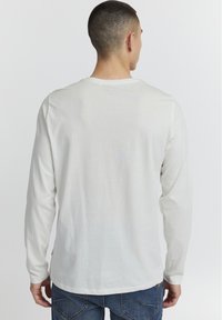 Langærmet skjorte i lysegr�å bomuld. Har en rund halsudskæring og en lige kant. Båret med blå jeans. Minimalistisk design, ingen mønstre.