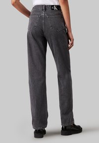 Šedé džíny z denimu se střihem rovného nohavice, viditelnými stehy, zadními kapsami a značkovou visačkou na pase. Hladký povrch a volný střih.