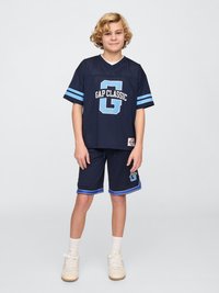 Jersey de malla marinera con el logo "GAP CLASSIC" en azul claro, acompañado de pantalones cortos a juego con rayas laterales. Zapatillas y calcetines blancos.