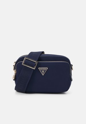 Mørkeblå crossbody taske med sølv lynlåse, justerbar bred rem og trekantet Guess-logo på fronten.