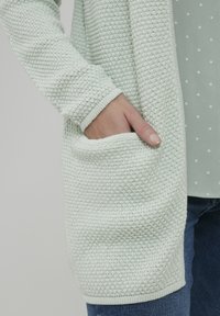 Cardigan lavorato a maglia in verde menta chiaro, con un motivo testurizzato, maniche lunghe, apertura frontale e una tasca frontale a toppa.