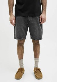 Camiseta negra de algodón combinada con pantalones cortos de mezclilla gris oscuro. Los pantalones cortos tienen un corte holgado, dobladillo deshilachado y bolsillos básicos. Zapatos de ante color arena y calcetines crema.