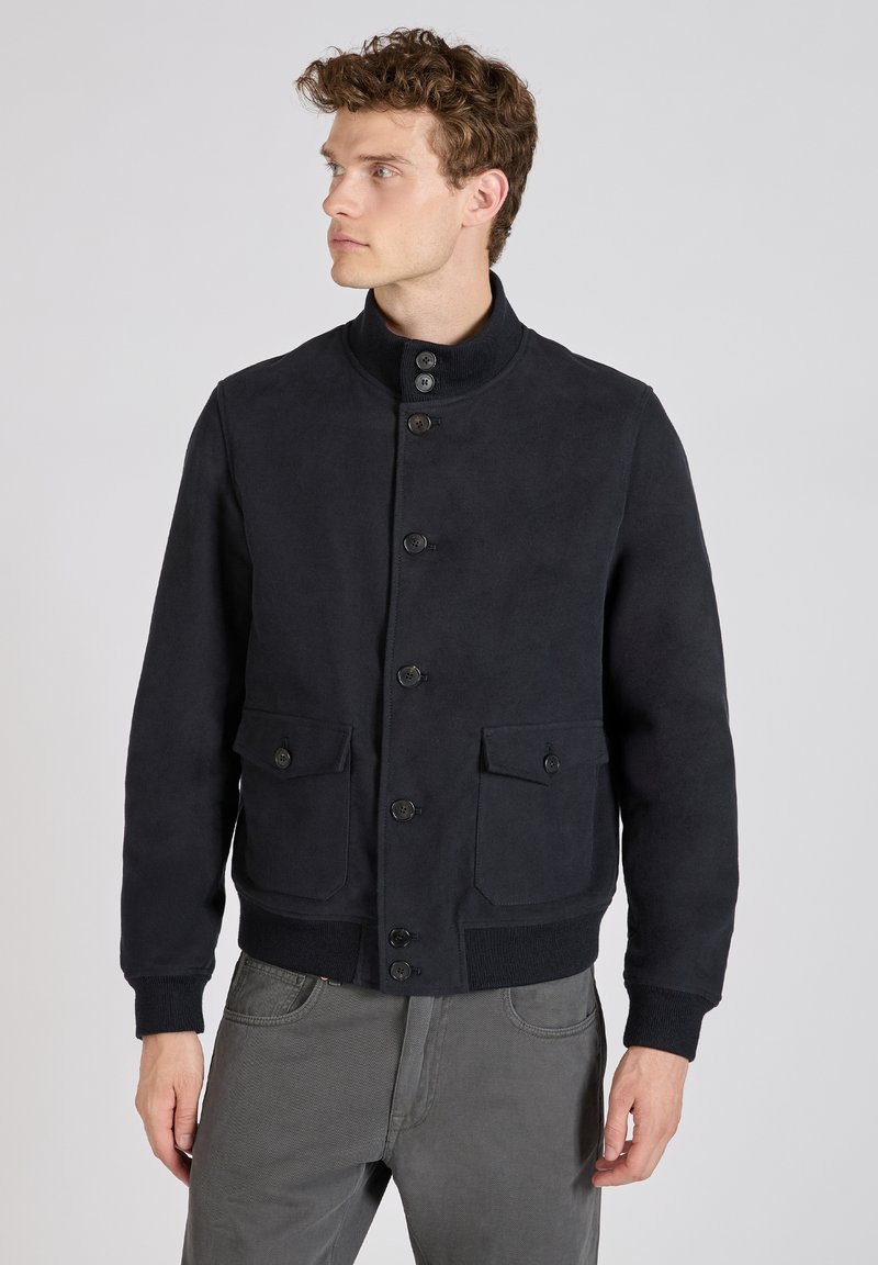 Navy blauwe jas met een hoge kraag, knoopsluitingen en twee voorkruizen. Gemaakt van een gladde, gestructureerde stof met ribbelboorden en zoom.