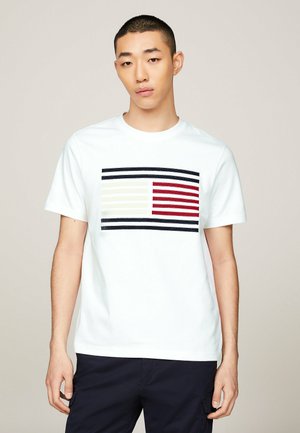 T-shirt bianca in cotone con un design rettangolare a strisce in nero, rosso e crema sulla parte anteriore. Colletto a girocollo e maniche corte.