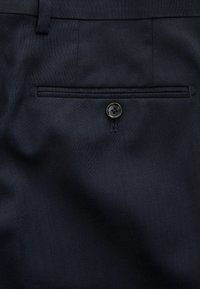 Pantalons navy avec une poche arrière plate et une fermeture à bouton sombre, fabriqués à partir d'un tissu texturé pour la durabilité.