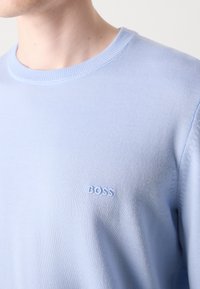 Pulôver de malha azul claro com decote redondo, apresentando um discreto logótipo bordado "BOSS" no peito. Textura suave e design ajustado.