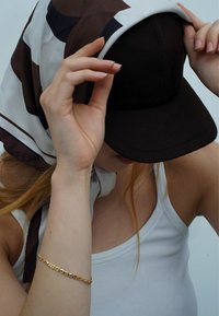 Brown felt cap worn under a patterned silk scarf. The scarf features dark brown and beige colors, showing smooth texture and soft draping.