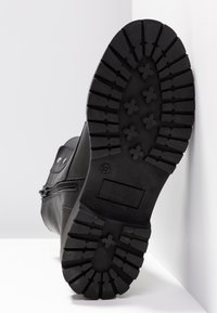 Semelle de botte en cuir noir avec un motif de semelle profond, comportant un design en zigzag et des grips en forme de croix pour l'adhérence. Matériau en caoutchouc solide.