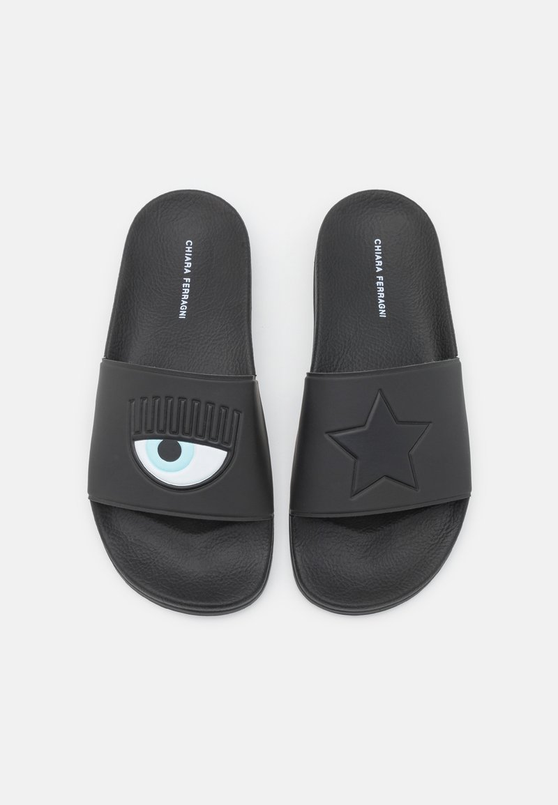 Schwarze Schslides mit Gummiriemen, wobei ein Riemen ein blaues Augendesign und der andere einen schwarzen Stern trägt. Der Text auf der Oberseite lautet "CHIARA FERRAGNI."