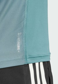 Vaaleansininen urheilupaita, jossa on teksturoitu kangas, ommeltu helma ja "ClimaCool+" -merkki. Yhdistetty mustiin shortseihin, joissa on valkoisia raitoja.