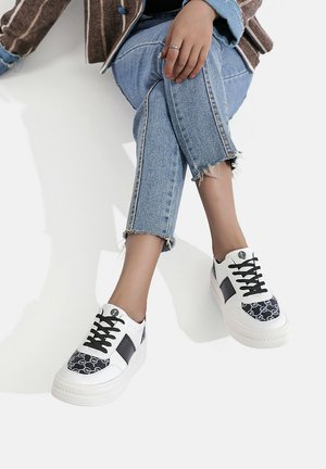Sneaker bianche con accenti neri e una punta in tessuto a motivo. Presentano lacci neri e una suola testurizzata. Abbinare a jeans blu sbiaditi.
