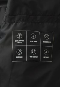 Schwarzer Stoff mit einem Etikett, das sechs Symbole und Text anzeigt, der die Eigenschaften angibt: recycelte Daunen und Federn, extra warm, wasserabweisend, atmungsaktiv, winddicht, leicht.