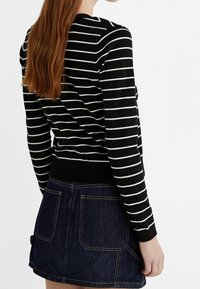 Zwart-wit gestreepte trui met lange mouwen, geribbelde zoom, gedragen over een denimrok met twee achterzakken en een donkerblauwe wassing.