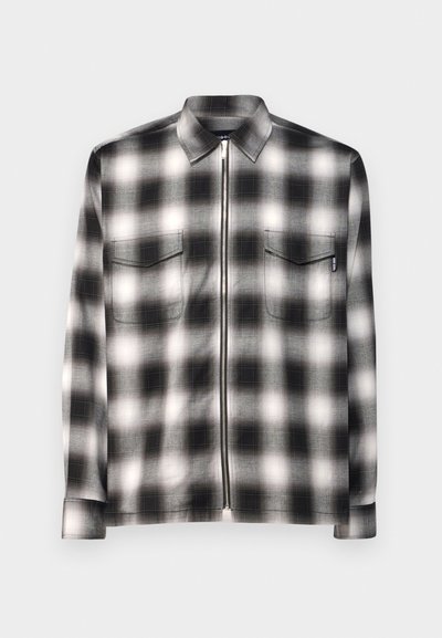 Black and white checkered shirt with a collar, long sleeves, two front pockets, and a full-length front zipper. Soft fabric texture.