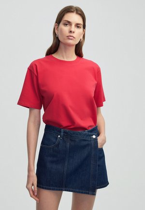 Rode katoenen T-shirt met korte mouwen, gecombineerd met een donkere denim rok met een zijzak en zilveren knoopdetails.