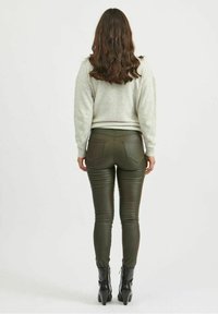 Harmaa neule ja oliivinvihreät mokkanahkavetimet, tiukka malli takataskuilla ja joustavalla kankaalla, yhdistettynä mustiin korkokenkiin.