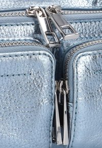Metalen blauwe neplederen tas met dubbele zilveren ritsen en een gestructureerd oppervlak, voorzien van contrasterende stiksels en twee ritscompartimenten.