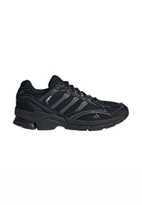 Baskets de sport noires avec tige en mesh, design à lacets, col rembourré et semelle épaisse en caoutchouc avec le logo trois bandes d'Adidas sur le côté.