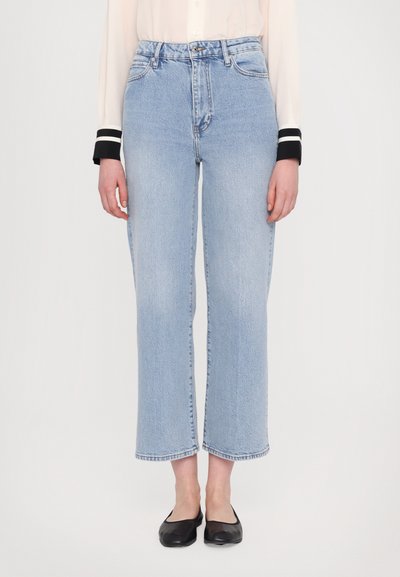 Un jean droit bleu clair avec une taille haute, des coutures visibles et des ourlets bruts. Associé à des chaussures plates noires pour le contraste.