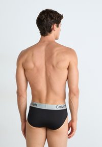 Schwarze Baumwollunterhose mit einem grauen elastischen Bund, der das "Calvin Klein"-Logo zeigt. Einfaches Design, glatte Textur, körpernahe Passform.