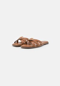 Brown leather slide sandals featuring wide straps, a rounded toe, and a decorative metallic accent. Flat sole with smooth texture.