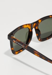 Tortoiseshell sunglasses with dark green lenses, angular design, and silver hardware detail on the temples. Brand name printed on the side.