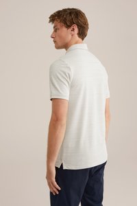 Svetlosivá polo košeľa s krátkym rukávom, textúrovaná látka, bočné rozparky a klasický golier. V kombinácii s tmavými nohavicami, zobrazené zozadu.