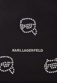 Čierny textil s kryštálovými ozdobami v tvare bublín a s názvom značky "KARL LAGERFELD" v striebornom kovovom prevedení.