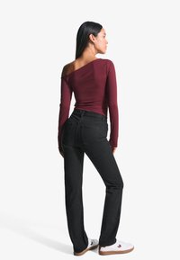 Burgundy long-sleeve top with an asymmetric neckline, paired with black straight-leg jeans and white sneakers with brown soles.