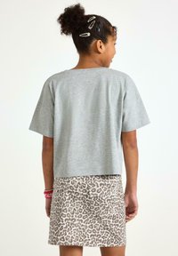 Grå kortärmad t-shirt kombinerad med en beige leopardmönstrad kjol. Outfiten har subtila sömmar och dekorativa accessoarer i håret.