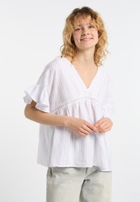Hvid kortærmet bluse med V-hals, strukturerede striber, broderede lace detaljer og bell-sleeves, parret med lyse denim jeans.