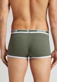 Olivově zelené pánské boxerky s ribrovou texturou, s bílým pasem s logem značky. Zadní pohled ukazuje těsné padnutí a krátkou délku.