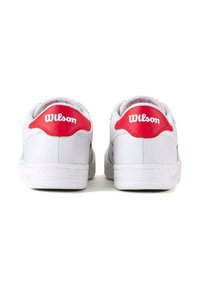 Baskets blanches avec une tige en cuir lisse, des accents rouges au talon et le logo "Wilson" en blanc à l'arrière. Semelle en caoutchouc plate.